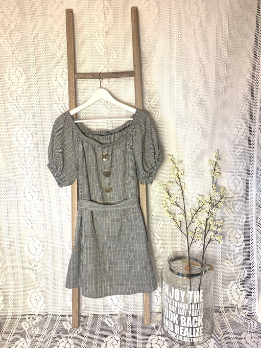 Kort kjole i rutemønster i grå, hvit og sort.Store blanke knapper foran til pynt og knyting i livet.Fremside.